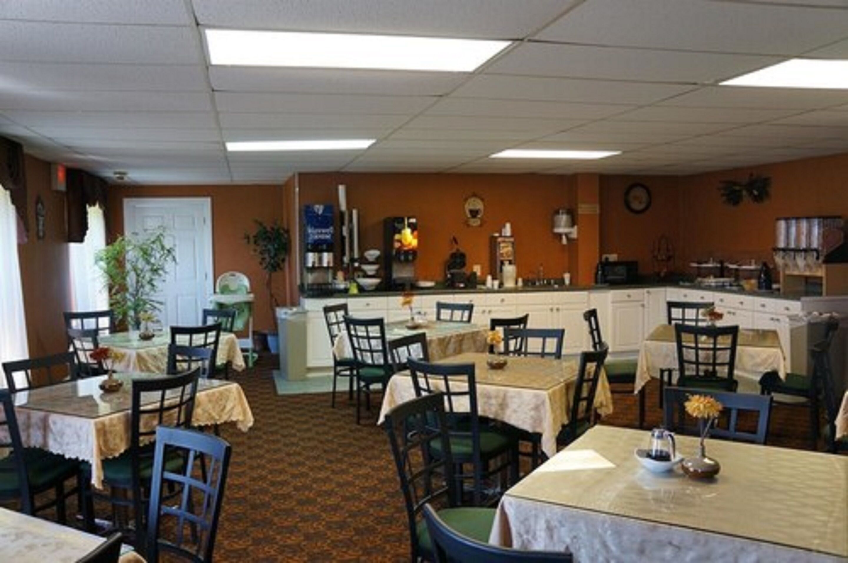 A dining area with tables and chairs, a kitchen area with appliances, and a clock on the wall.