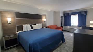A hotel room with a large bed, a desk, a chair, and a wardrobe.