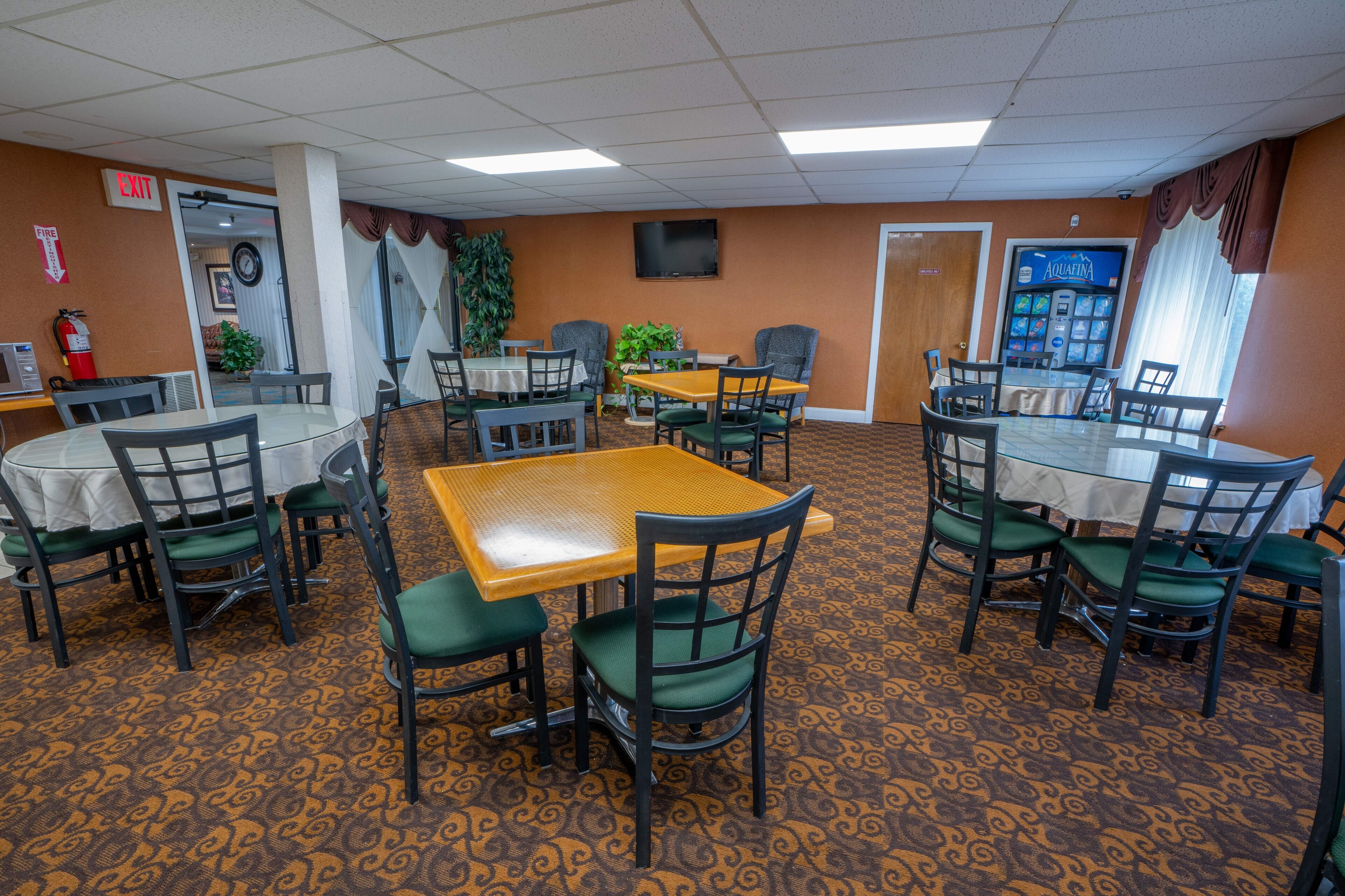 A conference room with tables and chairs, a fire extinguisher, and a television on the wall.