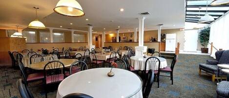 Un vaste espace dédié à la salle à manger, avec des tables et des chaises rondes, de grandes suspensions et un sol recouvert de moquette.