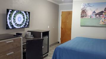 Una habitación de hotel con una cama, un escritorio con un ordenador, un televisor en la pared y un cuadro de un molino.