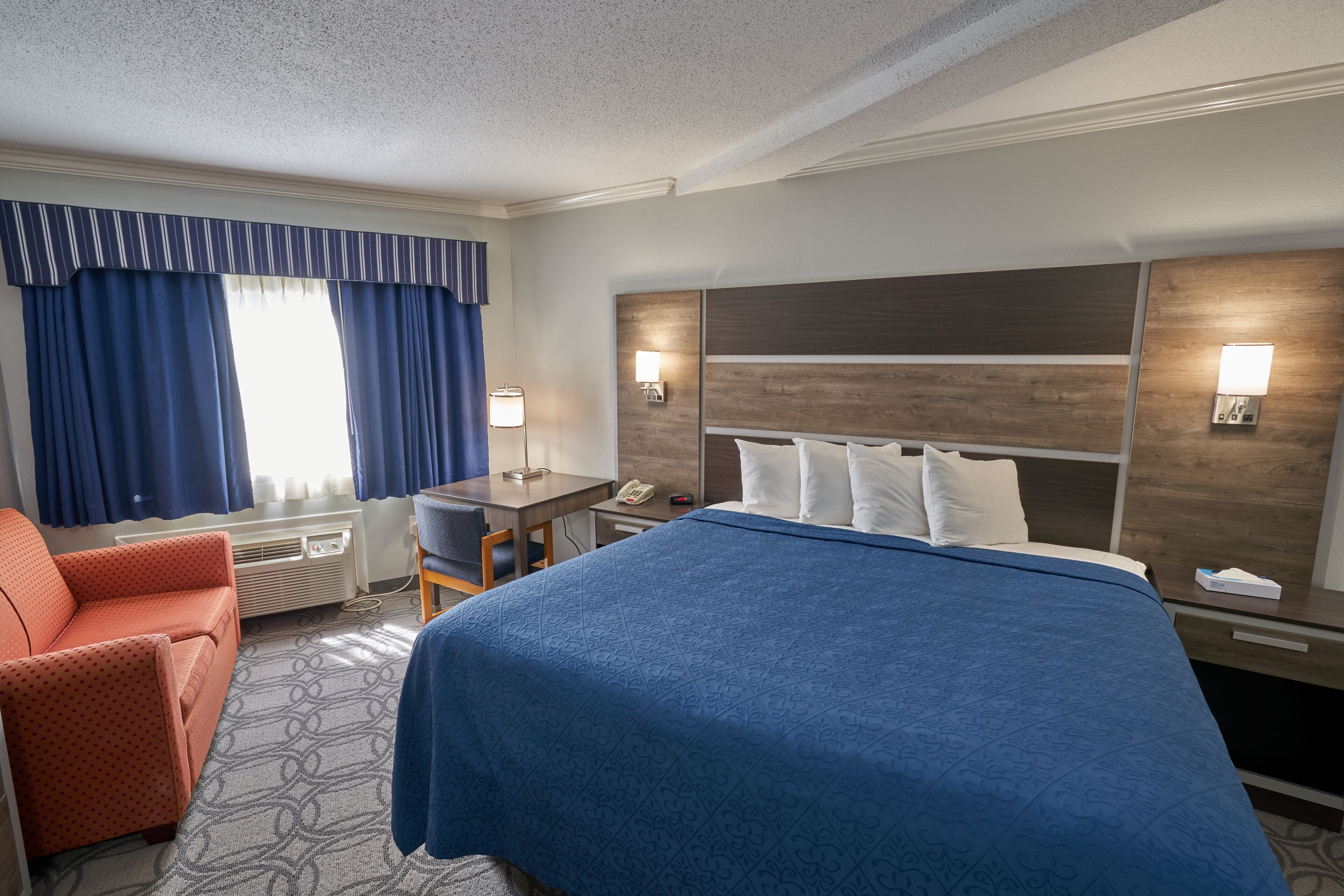 Quarto de hotel com uma cama grande, uma escrivaninha, uma cadeira e uma janela com cortinas.
