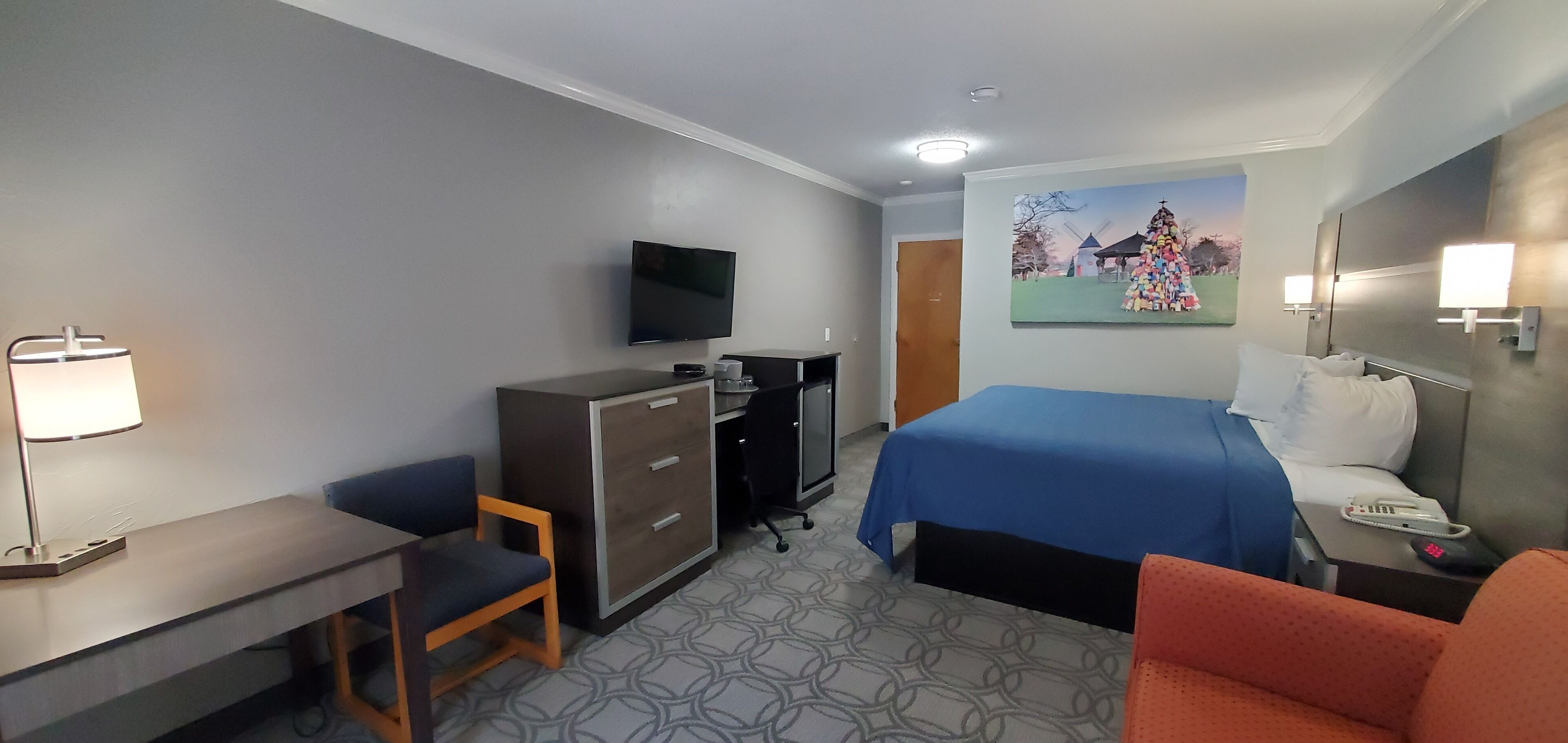 Une chambre d’hôtel avec un lit, un bureau, une chaise, une télévision et un tableau au mur.
