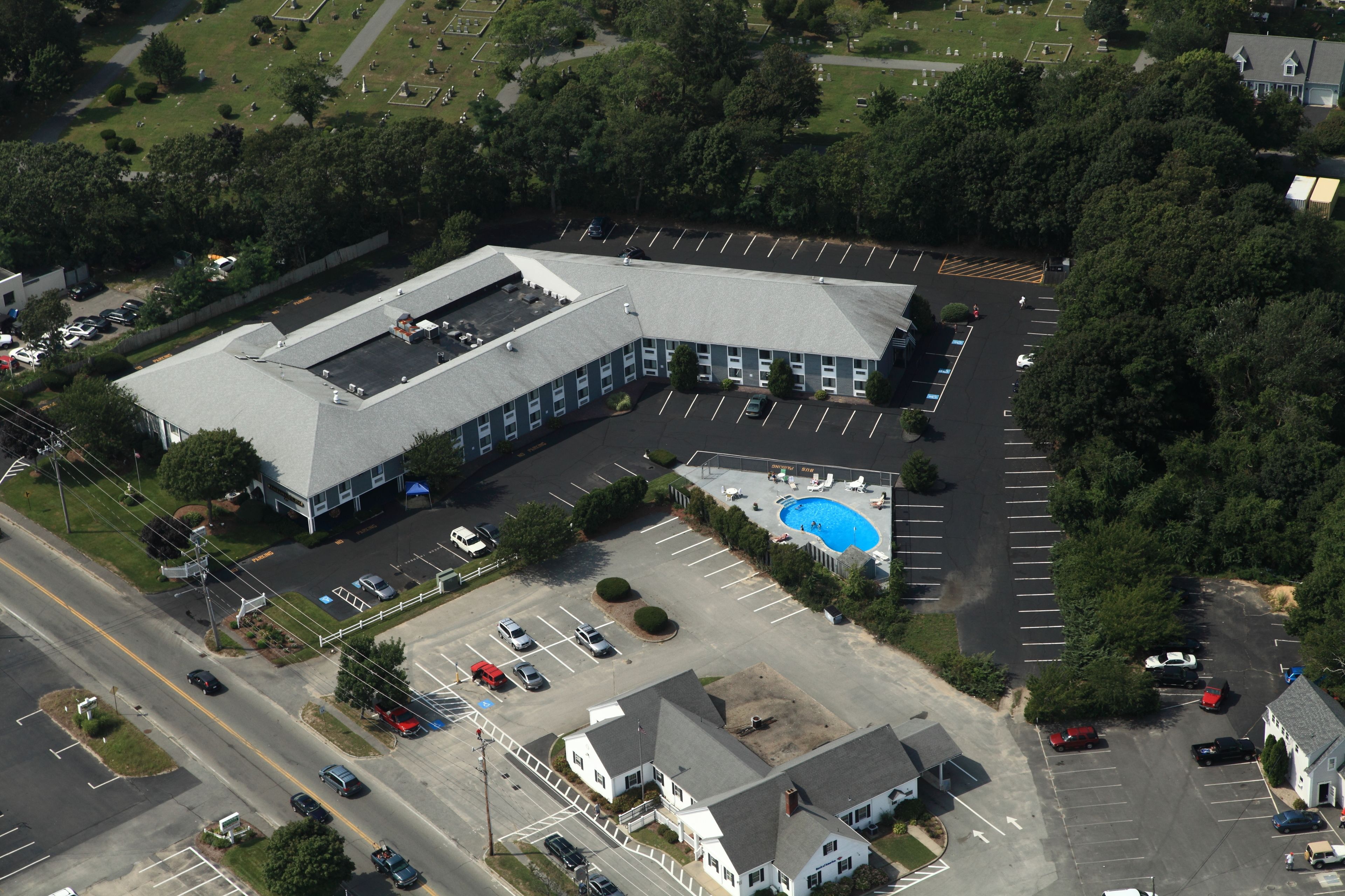 Ett flygbildsfoto av en stor byggnad med en parkeringsplats, en swimmingpool och en väg med fordon.