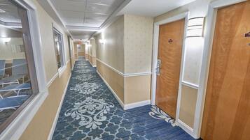 A hotel hallway with a patterned carpet, wooden doors, and a corridor leading to rooms.