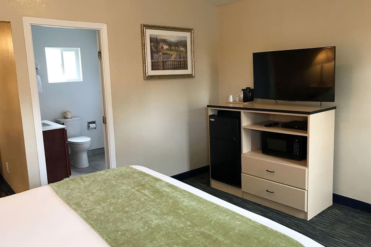 A hotel room with a bed, a television, a small refrigerator, a microwave, and a bathroom visible through an open door.