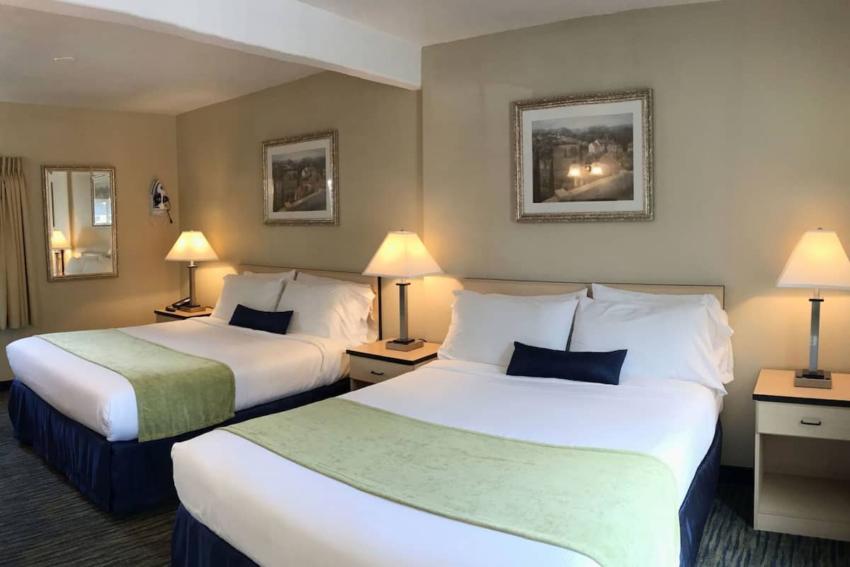 A hotel room with two beds, bedside lamps, a mirror, and framed pictures on the walls.