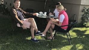 Two people seated at an outdoor table under a green umbrella, with a house in the background.