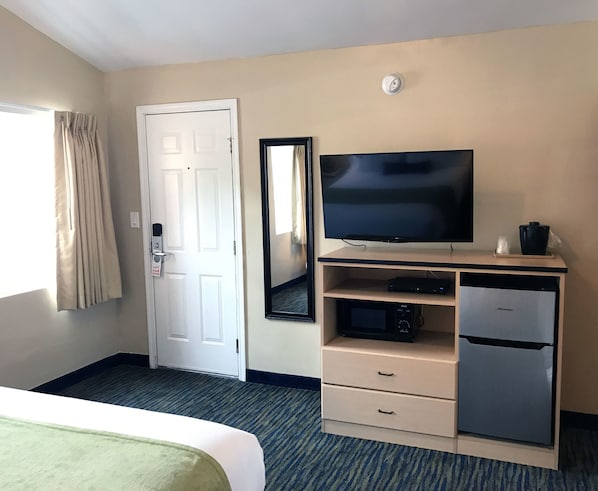 A hotel room with a bed, a television, a mirror, a refrigerator, and a door.