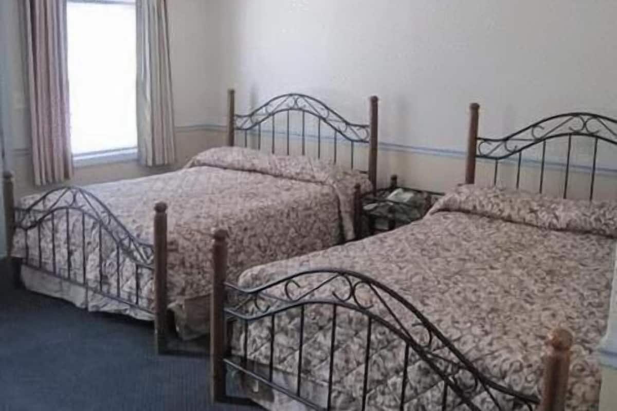 Una habitación con dos camas, cada una con estructura metálica y ropa de cama estampada con motivos florales.