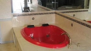 A red bathtub in a bathroom with beige tiles and a mirror above it. - Parsippany Inn and Suites Morris Plains (Morris Plains)