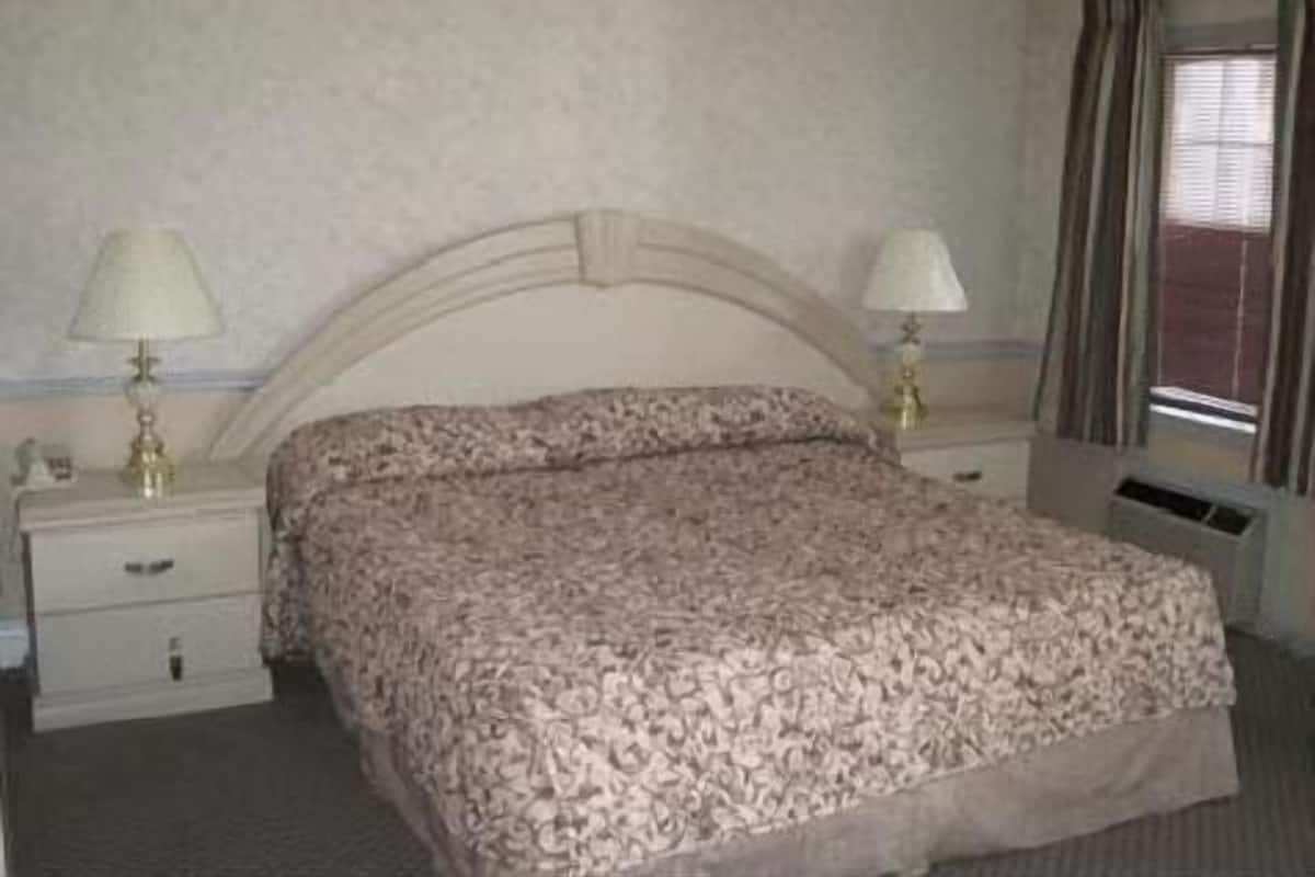 Una habitación de hotel con una cama, dos mesitas de noche, una lámpara en cada una y un ventanal con cortinas.