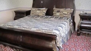 A bedroom with a wooden bed, patterned bedding, and a red carpet. - Parsippany Inn and Suites Morris Plains (Morris Plains)
