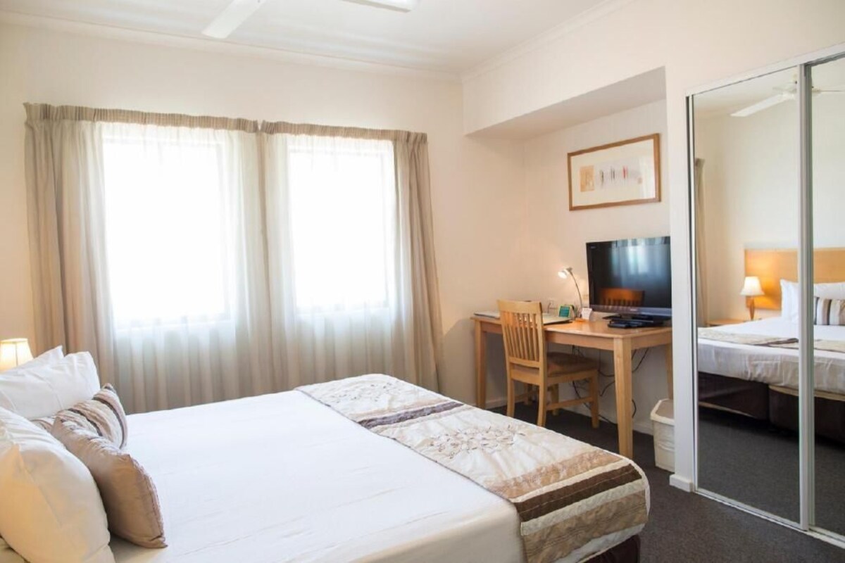 A hotel room with a bed, a desk with a chair, a television, and a sliding door leading to a bathroom.