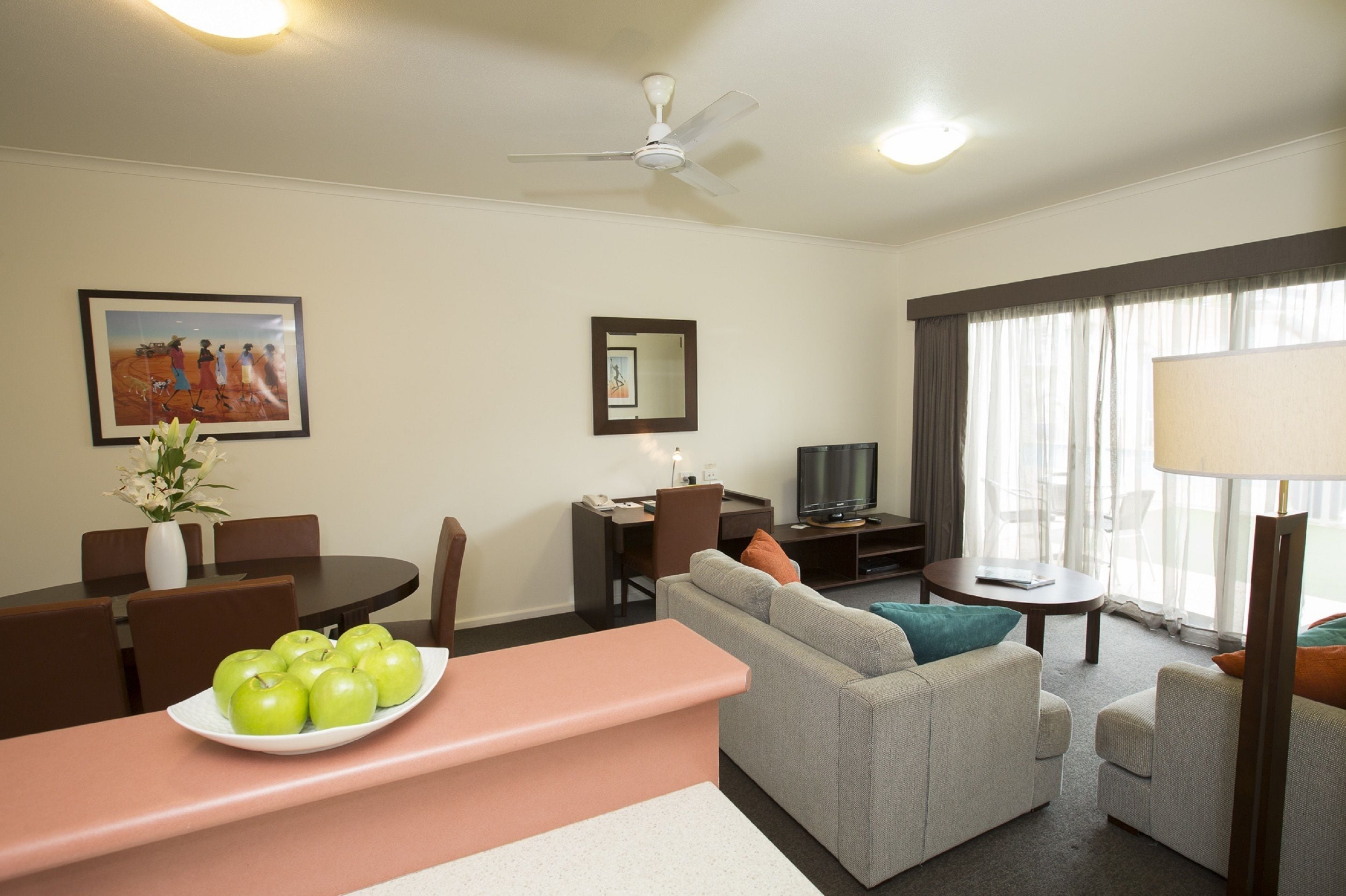 Quarto de hotel com sofá, mesa de jantar com cadeiras, televisão e ventoinha no teto.