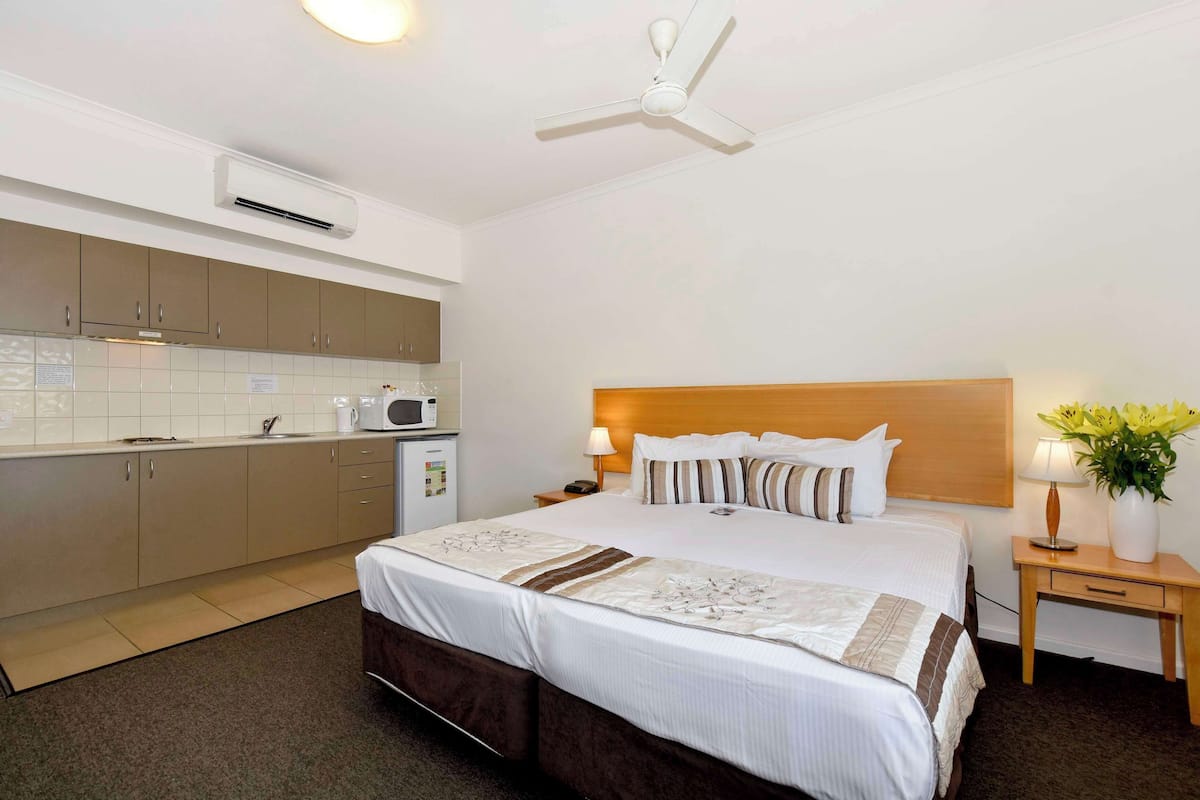 A hotel room with a bed, bedside table, lamp, and a small table with a vase of flowers.