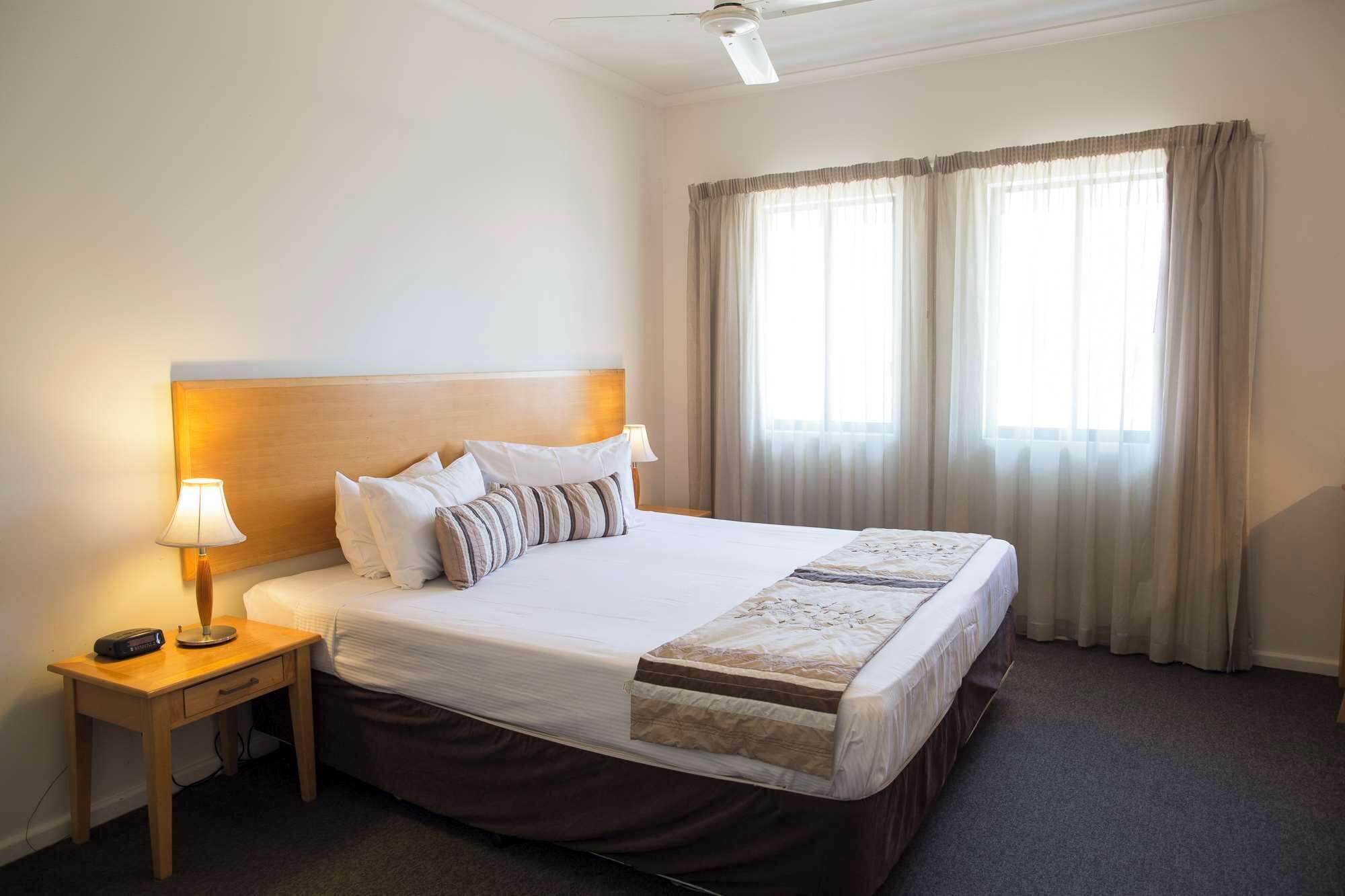 Une chambre d’hôtel avec un grand lit, une table de chevet avec une lampe et un ventilateur de plafond.