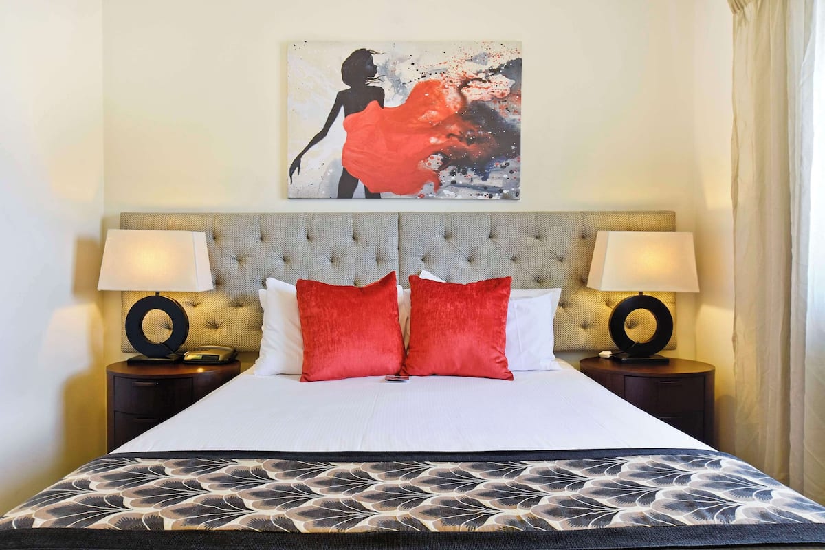 A neatly made bed with a patterned bedspread, two red pillows, and a headboard with a tufted design.