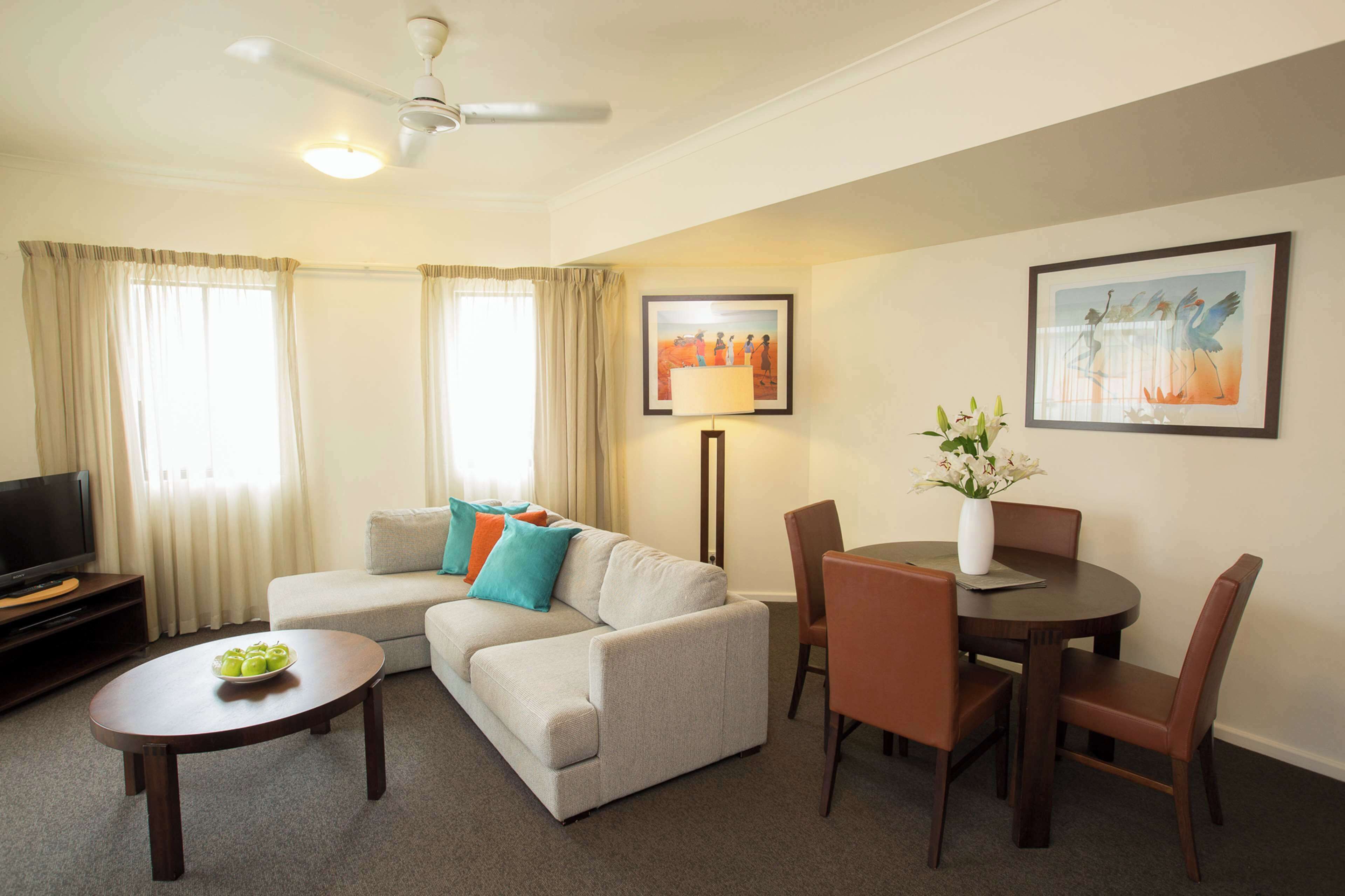 A living room with a sofa, coffee table, dining table with chairs, a TV stand, and artwork on the walls.