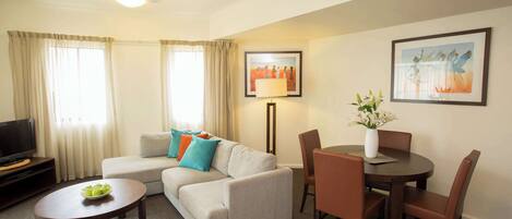 A living room with a sofa, coffee table, dining table with chairs, a TV stand, and artwork on the walls.