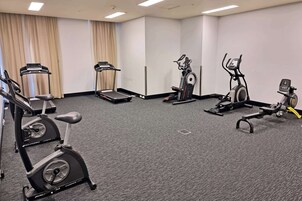 Gimnasio de hotel con máquinas de cardio, incluyendo cintas de correr y una elíptica, además de una pequeña plataforma elevada.