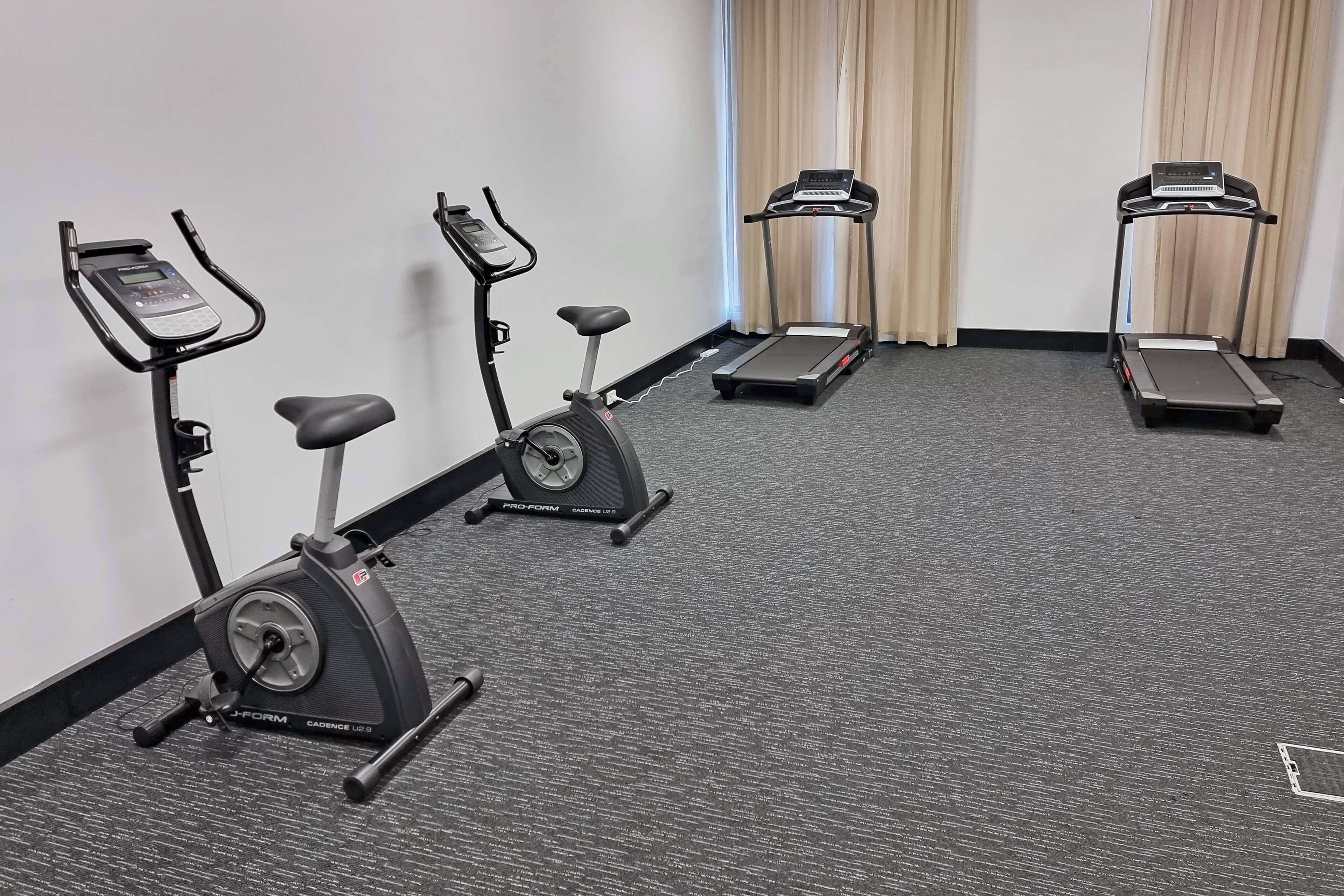 A fitness room with three stationary bikes, two treadmills, and a wall-mounted screen.