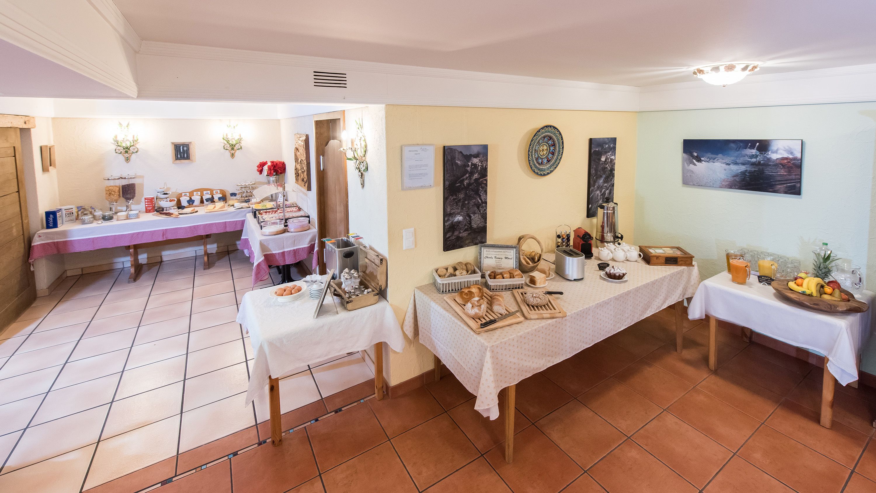 A dining area with multiple tables set for breakfast, featuring bread, pastries, and beverages.