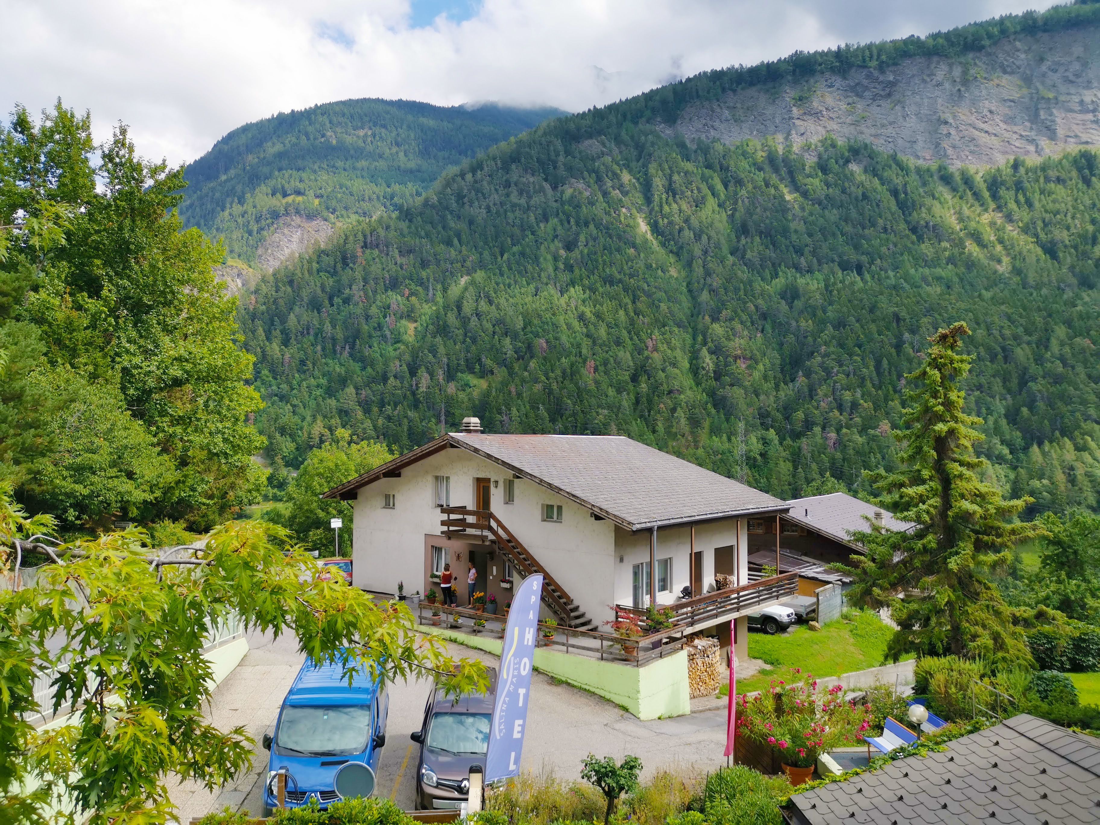 A hotel with a mountain backdrop, a parking area, and a staircase leading to the entrance.