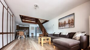 Een moderne woonkamer met een houten trap, een bank, een eethoek en een keuken op de achtergrond.