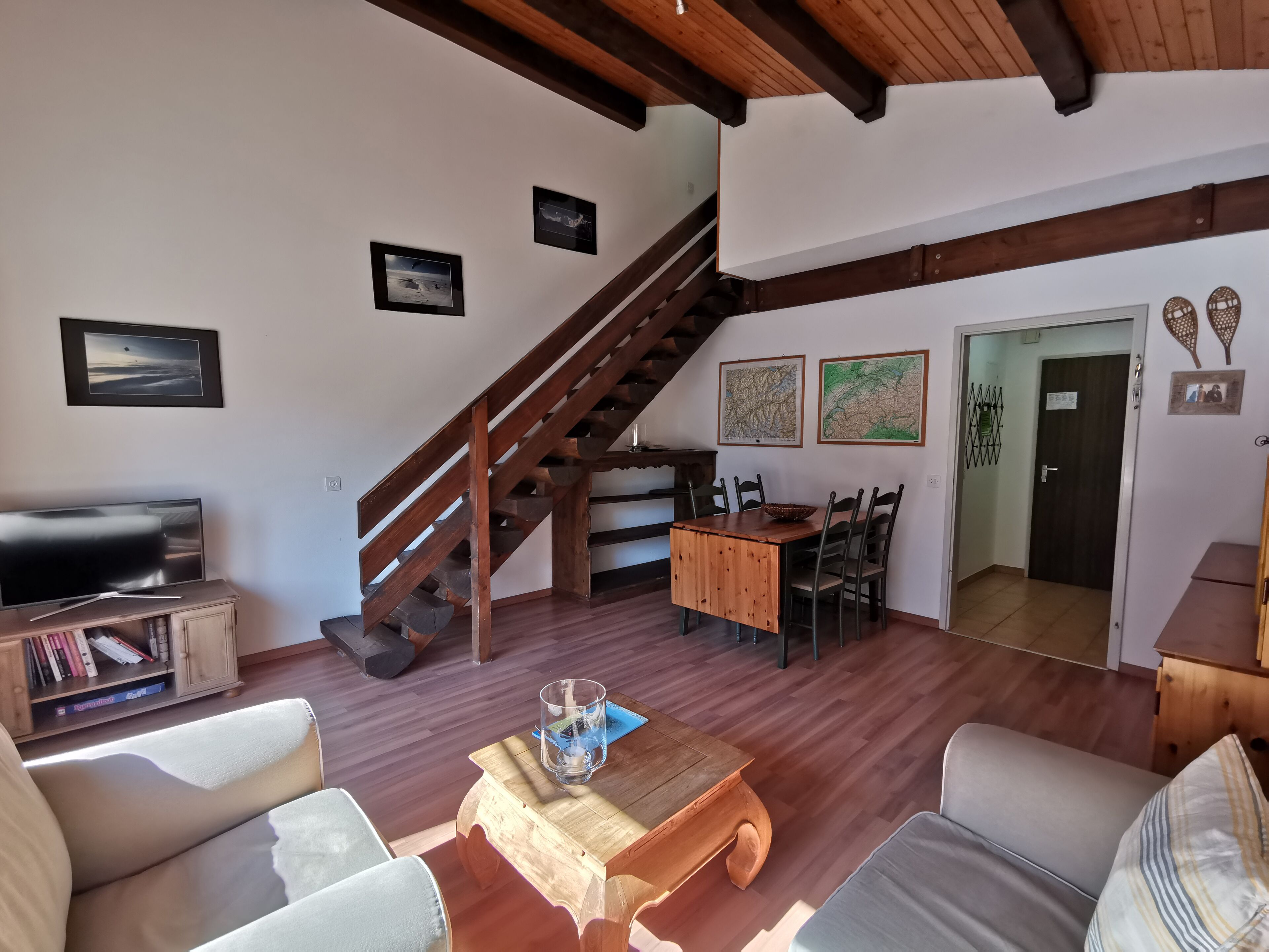 Un salon chaleureux avec un escalier en bois, une table à manger avec des chaises, un téléviseur et une bibliothèque.