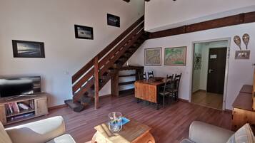 Un salon chaleureux avec un escalier en bois, une table à manger avec des chaises, un téléviseur et une bibliothèque.