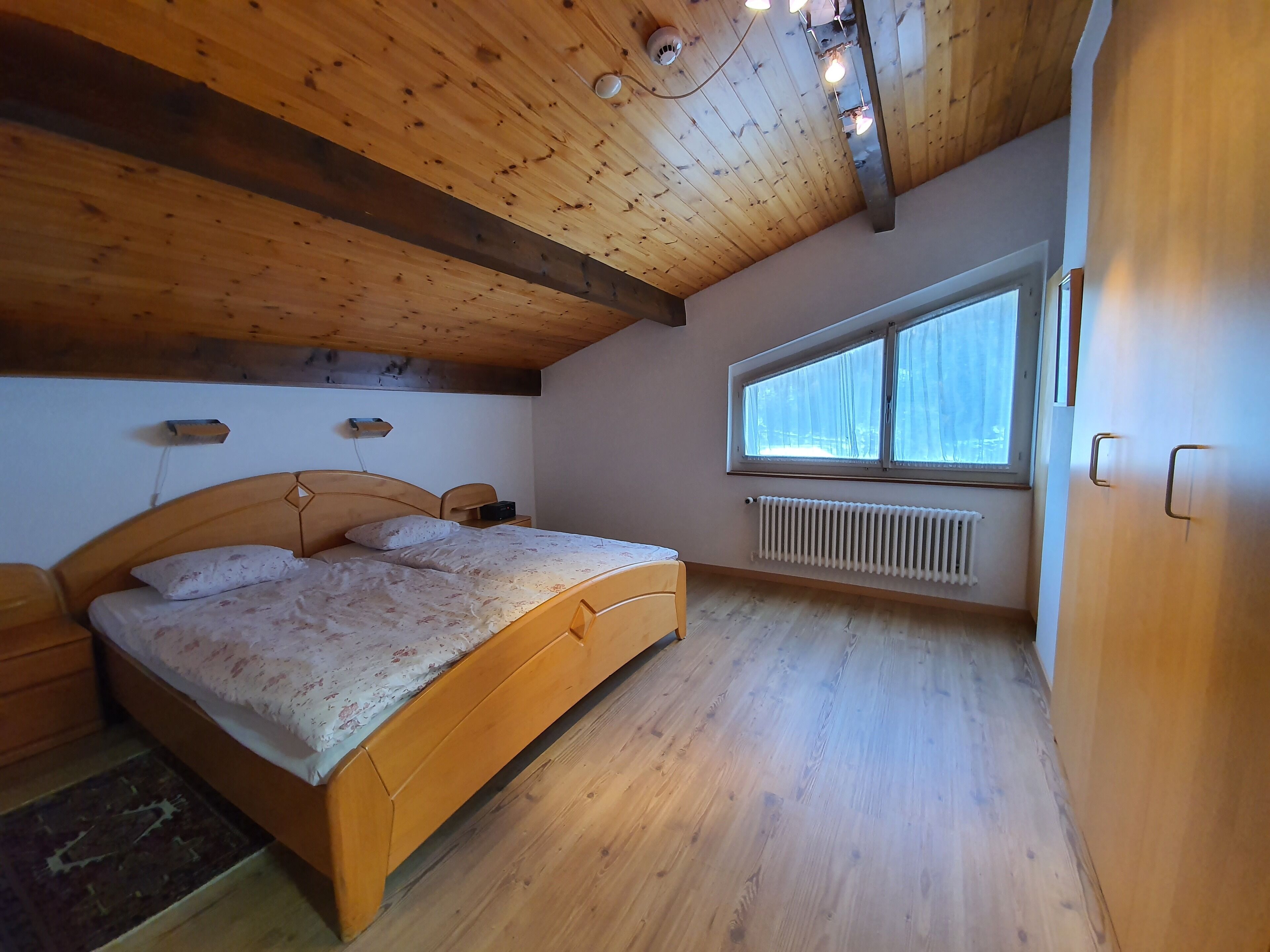 Ein Schlafzimmer mit Holzboden, einem großen Fenster, einem Bett und einer Heizung.