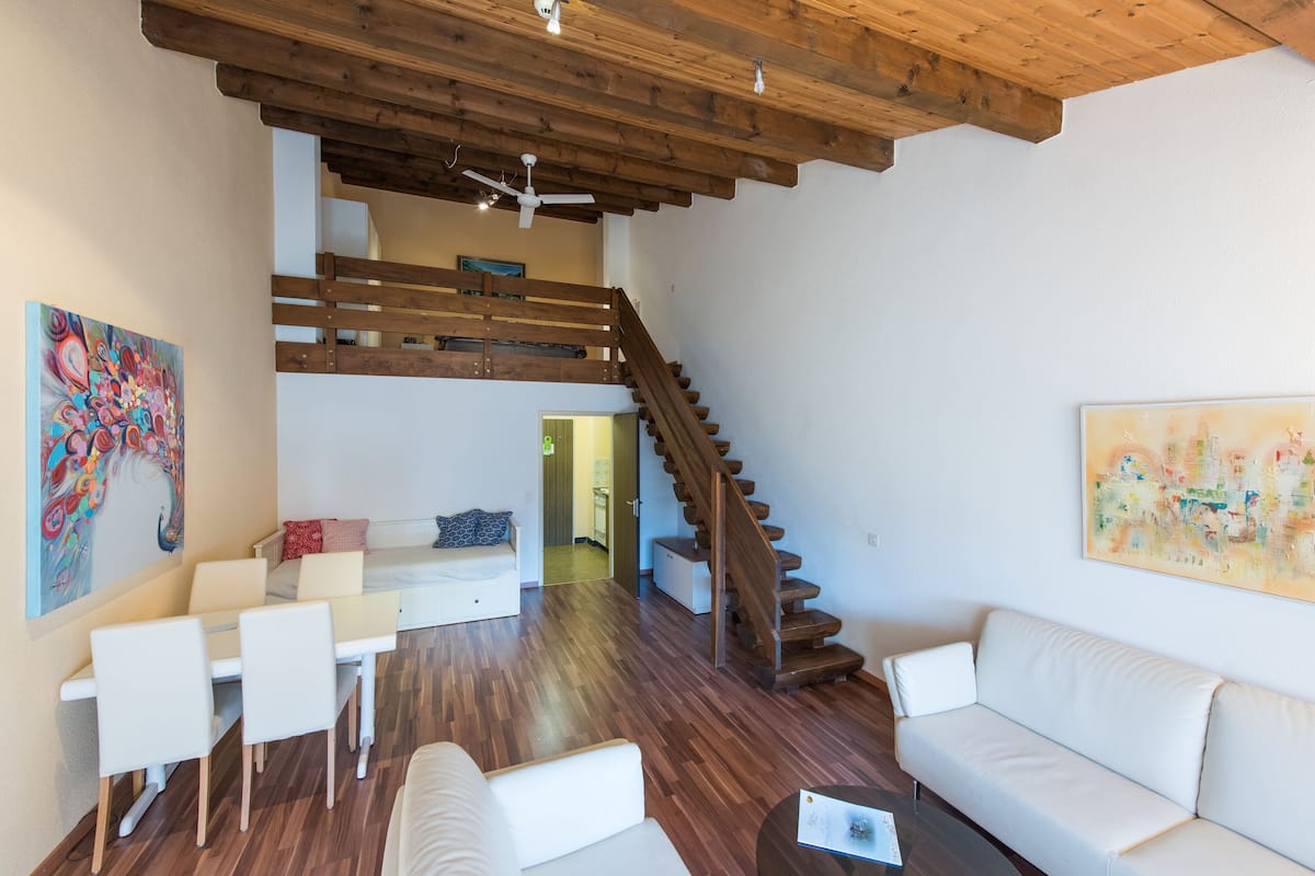 A spacious living area with a wooden staircase, white sofas, and a dining table.