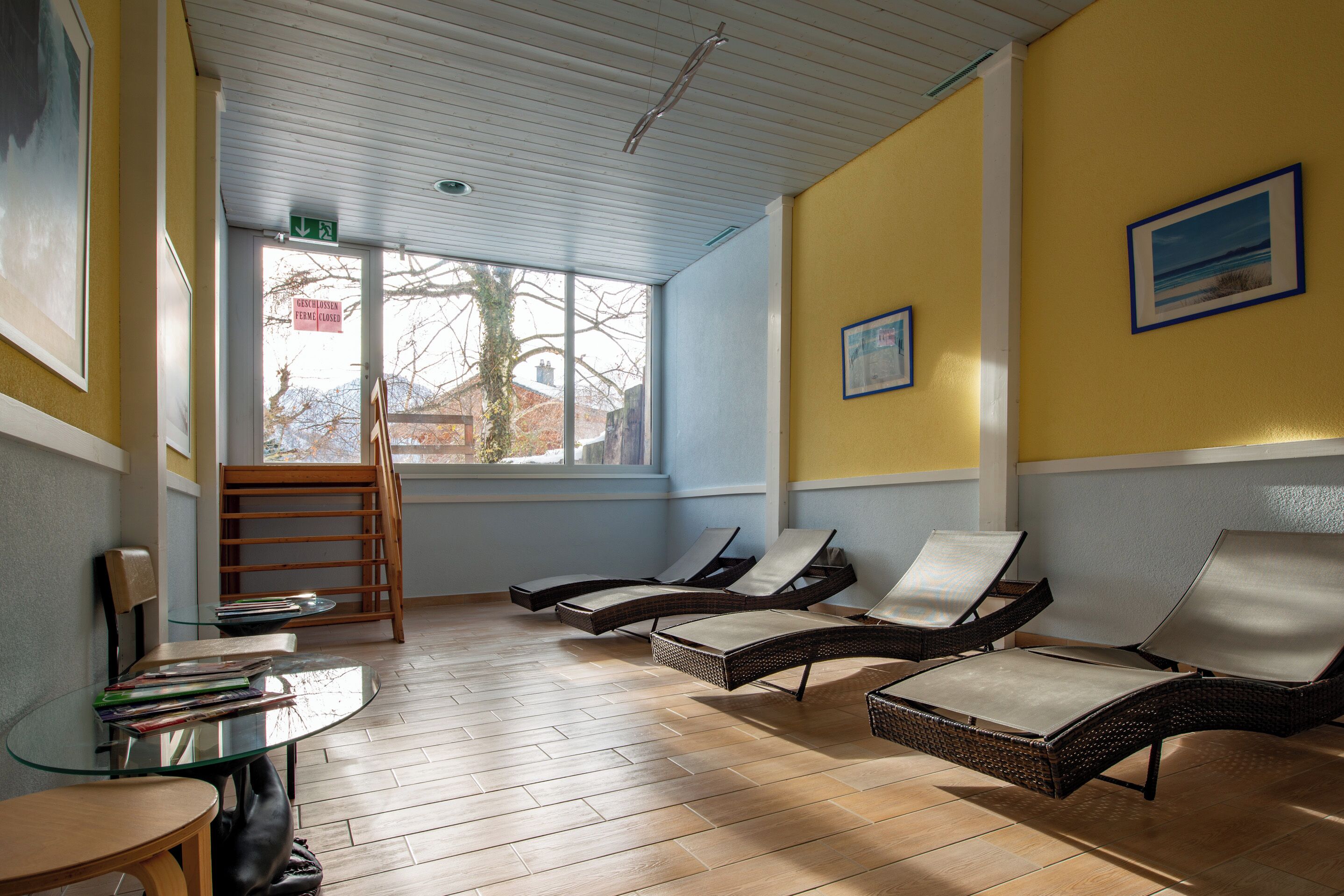 Una habitación iluminada por el sol con sillones de mimbre, una mesa de vidrio y vistas al exterior.