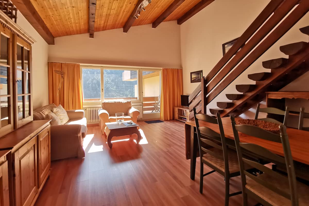 A spacious living room with a wooden staircase, a sofa set, a coffee table, and a view of the outdoors.