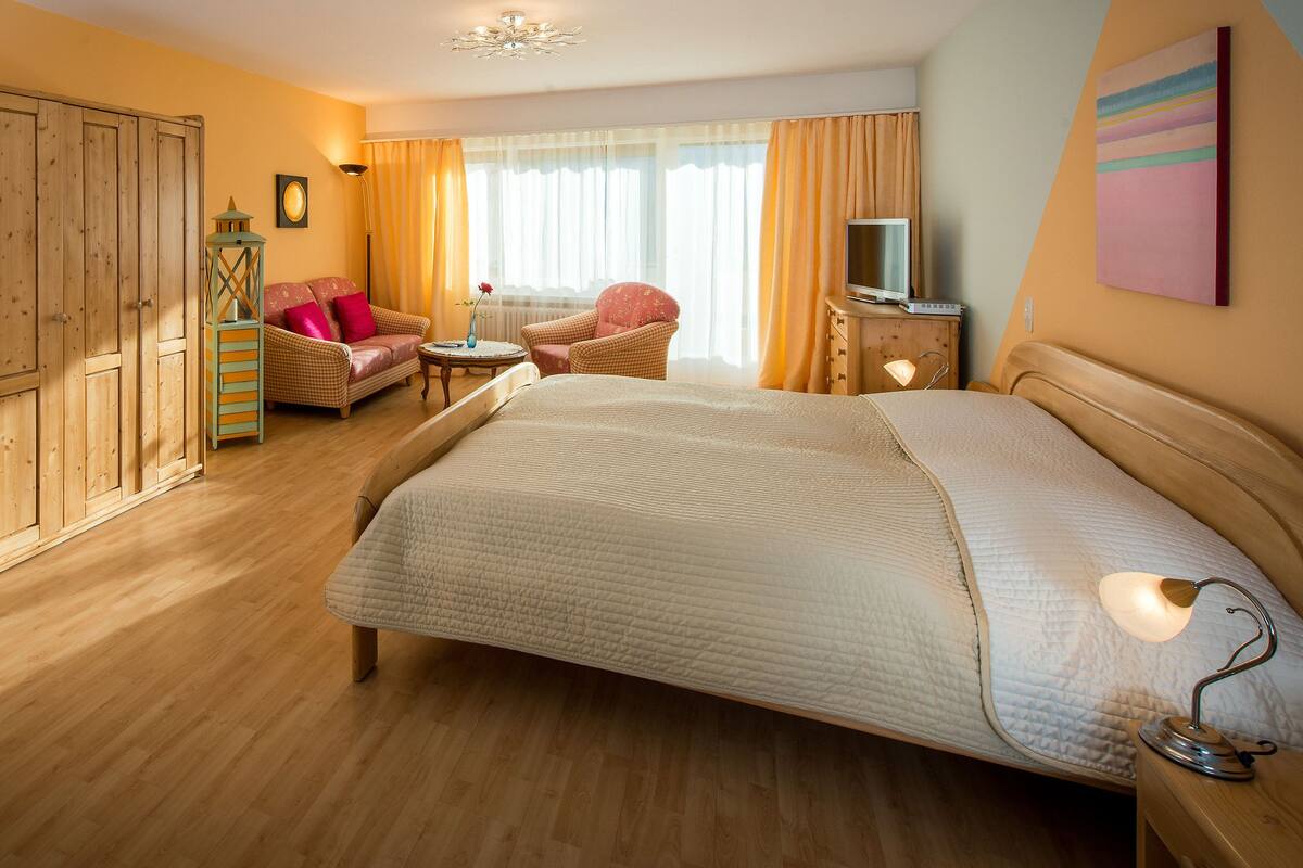 A hotel room with a large bed, a wardrobe, a seating area with a chair and a table, and a television on a wooden cabinet.
