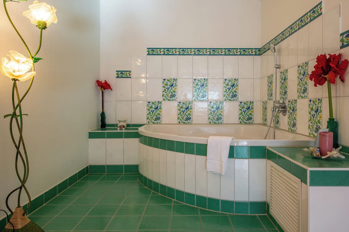 A bathroom with a freestanding bathtub, green and white tiles, a shower, and a vase with red flowers.