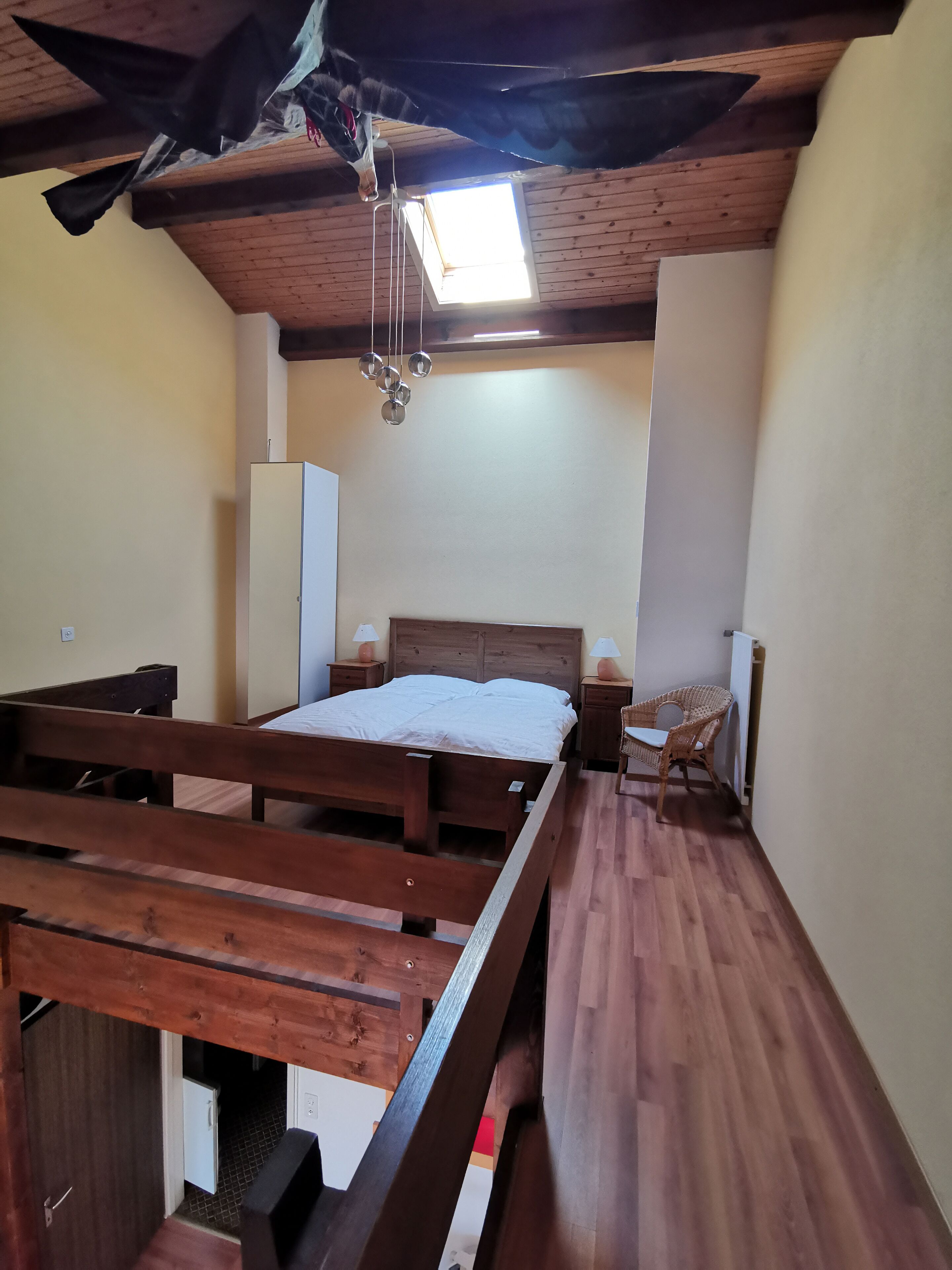 A bedroom with a wooden bed, a nightstand, a wicker chair, and a ceiling fan.