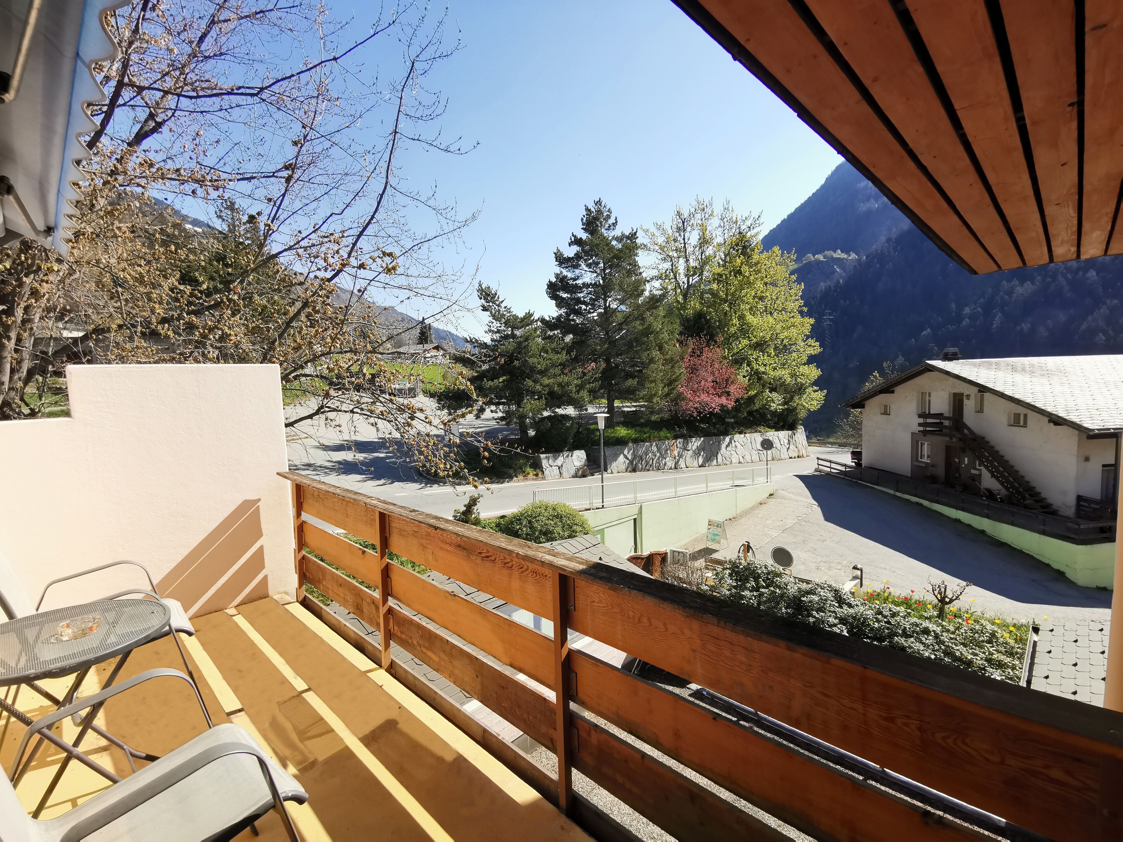 Een balkon met uitzicht op een berg, een klein gebouw en een verhard gebied met een hek.