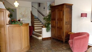 A wooden reception desk, a staircase, a red armchair, and a floor lamp. - Beaune Hotel (Beaune)