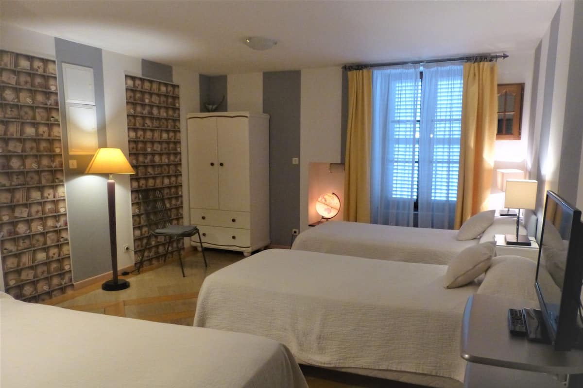 A hotel room with two beds, a wardrobe, a desk with a lamp, a small table, and a bookshelf.