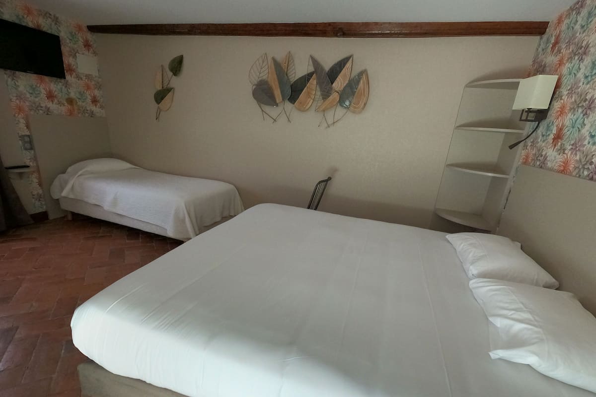 A bedroom with a large bed, two smaller beds, a wooden headboard, a wall-mounted shelf, and a decorative leaf artwork.