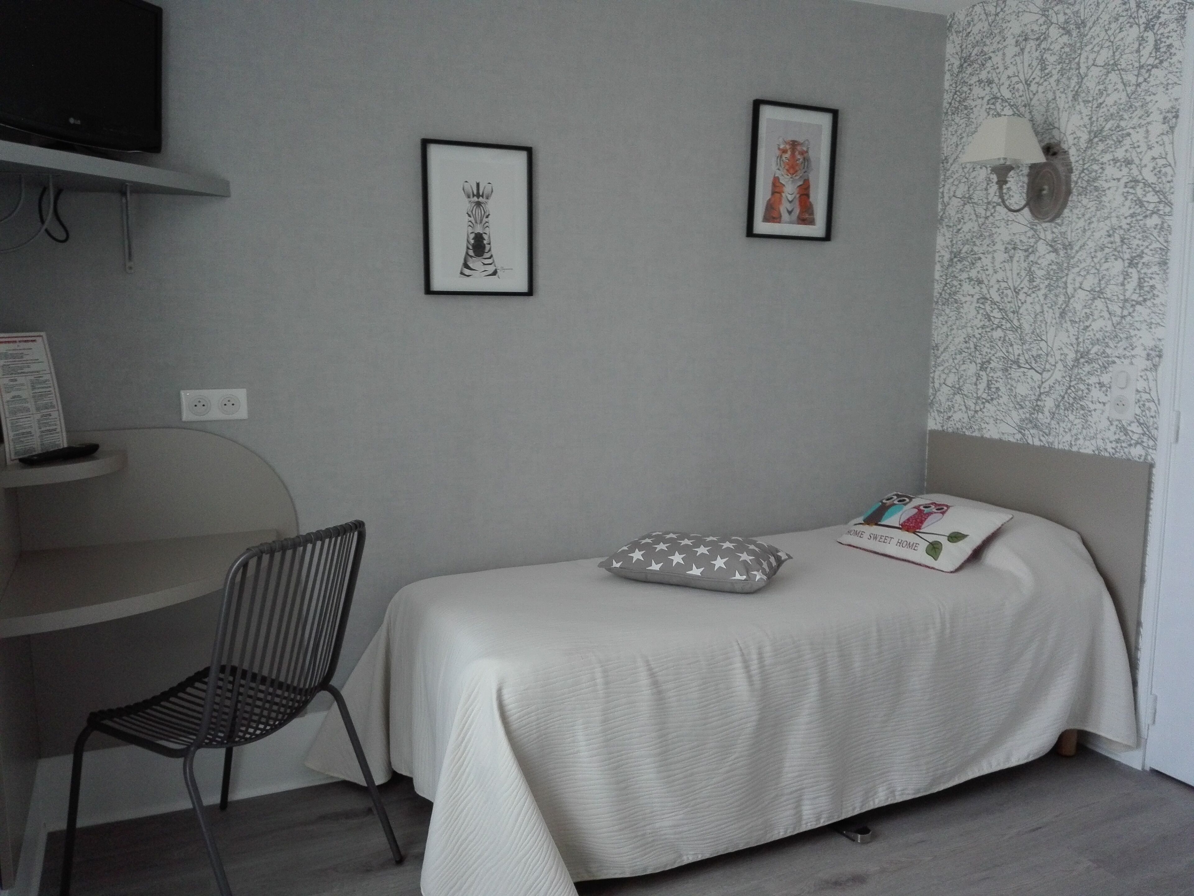 A bedroom with a bed, a chair, a desk, and two framed pictures on the wall.