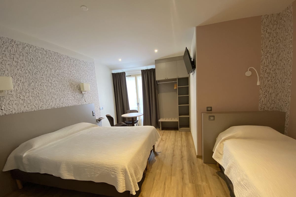 A hotel room with two beds, a desk, a chair, a wardrobe, and a television.