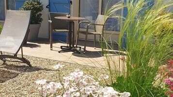 A patio area with a table and chairs, a sun lounger, and a potted plant.