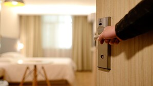 A hand turning a door handle in a hotel room with a bed and a lamp in the background. - Beaune Hotel (Beaune)
