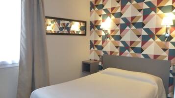 A hotel room with a bed, a nightstand, a wall-mounted lamp, and a geometric-patterned wall.