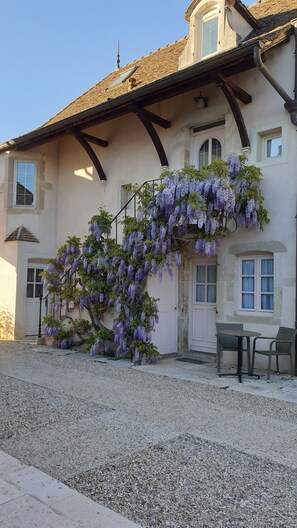 A building with a stone facade, a sloped roof, and a hanging purple flower wall. - Beaune Hotel (Beaune)