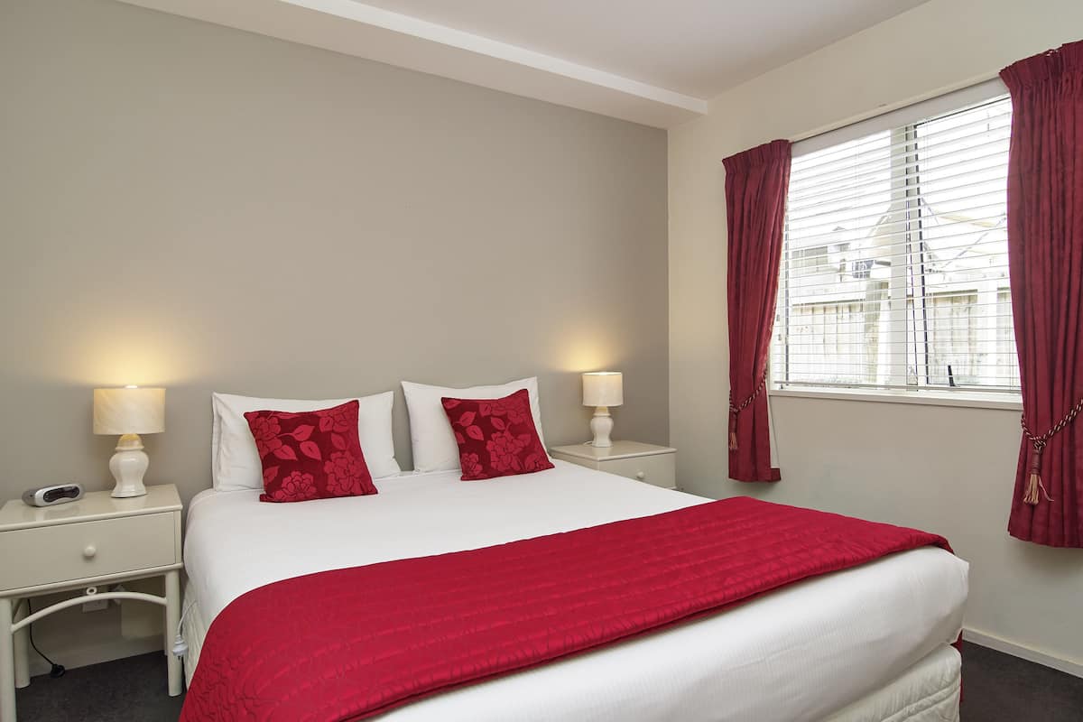 Une chambre à coucher bien rangée, avec un grand lit, deux tables de chevet avec des lampes et une fenêtre avec des rideaux.