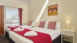 Ein Hotelzimmer mit zwei Betten, roter und weißer Bettwäsche, einem Bild an der Wand und einem Fenster mit Jalousien.